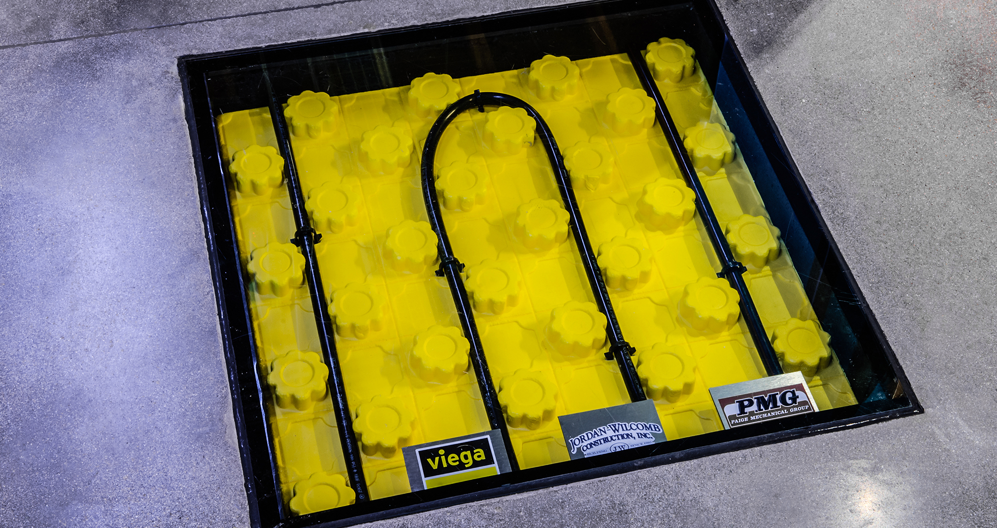 A glass floor window at CSHQA’s Boise office reveals PEX tubing in yellow insulated panels beneath the polished concrete floor.