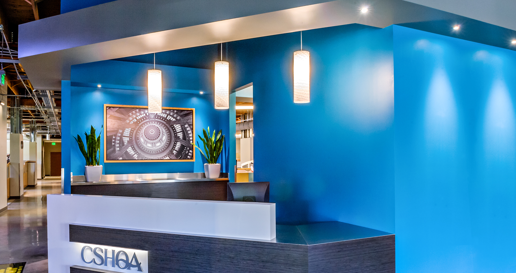 Reception desk at CSHQA’s Boise office with a bold blue wall, pendant lighting, and polished concrete floors.